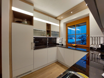 Moderne grifflose Einbauküche, weiße supermatt Lackfronten mit Anti-Fingerprint-Beschichtung, Arbeitsplatte & Rückwand Granit, Oberschrankbeleuchtung und LED-Griffmuldenbeleuchtung.