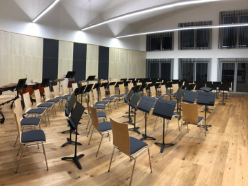 Orchesterproberaum mit Akustikpaneelen aus Holz für Wand und Decke. Integrierte Stauraummöbel mit gelochten Akustik-Schrankfronten Ahorn furniert.