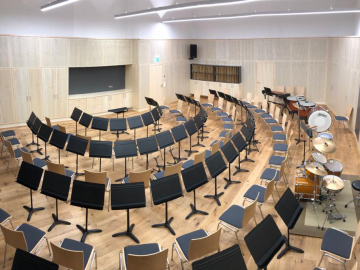 Orchesterproberaum mit Wand und Decken Akustikpaneelen. Integrierte Stauraummöbel mit gelochten Akustik-Fronten Ahorn furniert.